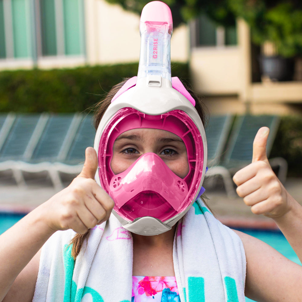 Child in pink G2RISE snorkel mask by pool, showing thumbs up for snorkeling fun.