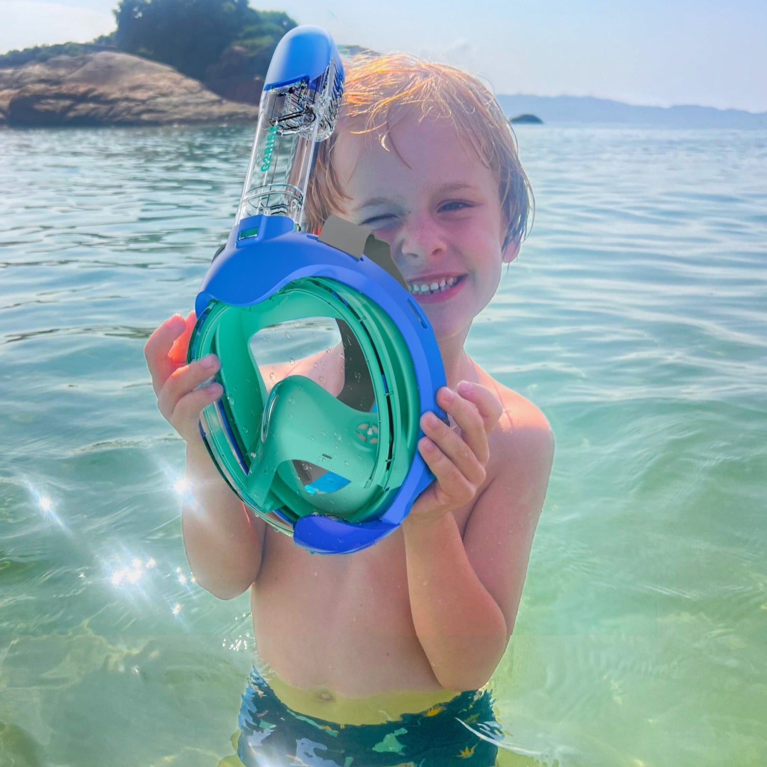 Boy holding blue-green G2RISE snorkel mask in clear water